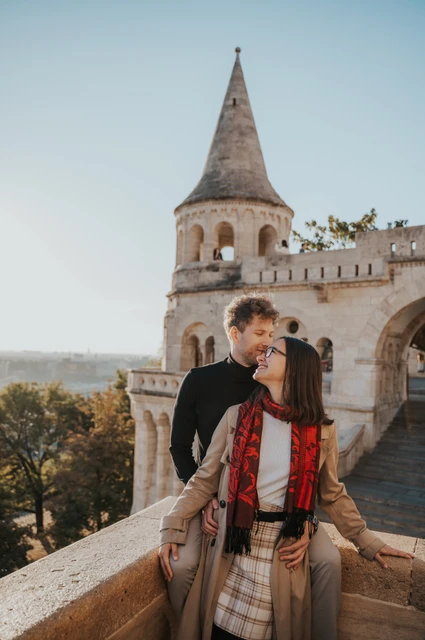 Budapest couple photoshoot: a kiss beside the pointed tower The man kissing his partner near her temple beside Fisherman’s Bastion’s stone balustrade during a couple photoshoot in Budapest.