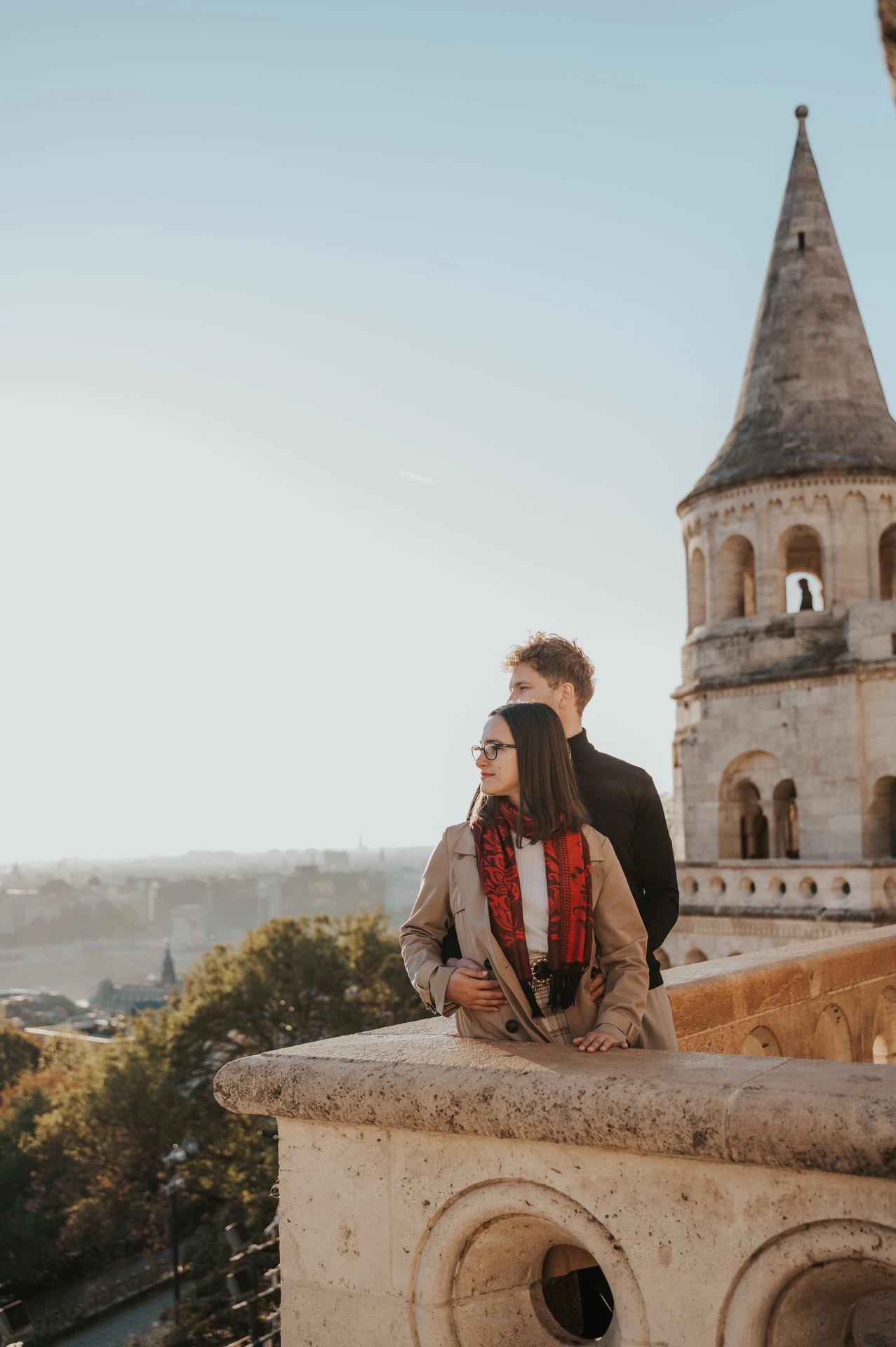 The couple beside a carved stone balcony with a pointed tower and city views at Fisherman’s Bastion during a couple photoshoot in Budapest.