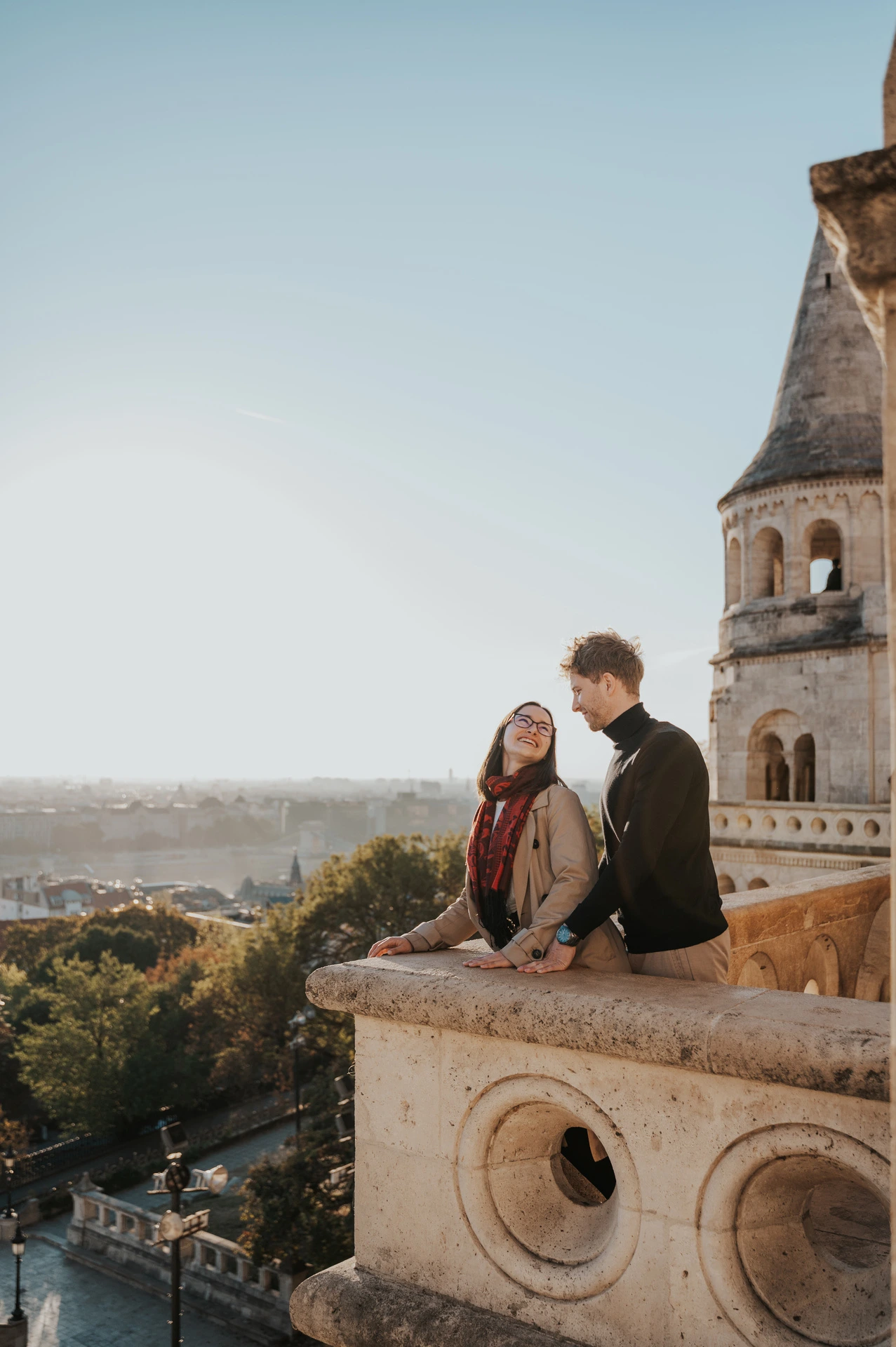 The woman leaning back towards her partner beside Fisherman’s Bastion’s carved balcony during a couple photoshoot in Budapest.