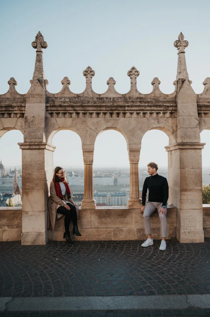 Budapest couple photoshoot: Parliament framed by a stone arch The couple on opposite sides of a stone archway at Fisherman’s Bastion, with Parliament across the Danube during a couple photoshoot in Budapest.