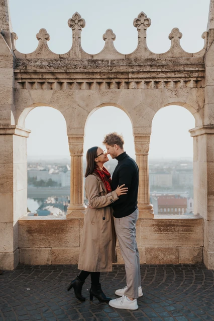 Budapest couple photoshoot: an embrace beneath the carved arches The couple embracing beneath Fisherman’s Bastion’s carved arches with the river and city behind them during a couple photoshoot in Budapest.