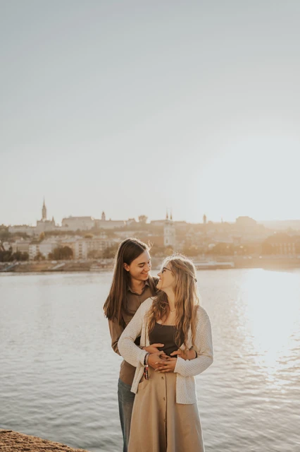 Budapest photoshoot with the Danube and evening sky in the backdrop A wider portrait of the couple holding each other close by the river during their Budapest photoshoot, with open sky and evening light around them.
