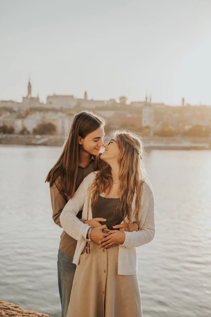 Budapest photoshoot sharing a look in soft riverside light The couple looking towards each other while embracing during their Budapest photoshoot by the river, with soft sunlight on their hair.