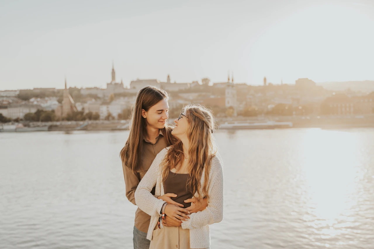Budapest couple photoshoot with golden river light in the backdrop The couple smiling together in a close embrace during their Budapest photoshoot, with golden light across the river behind them.