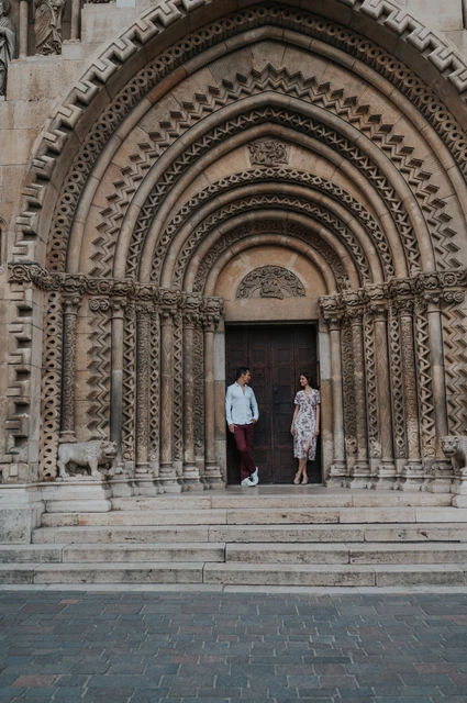 A grand castle doorway at a Budapest couple photoshoot The couple standing beneath the deeply carved arched doorway at Vajdahunyad Castle during their couple photoshoot in Budapest.