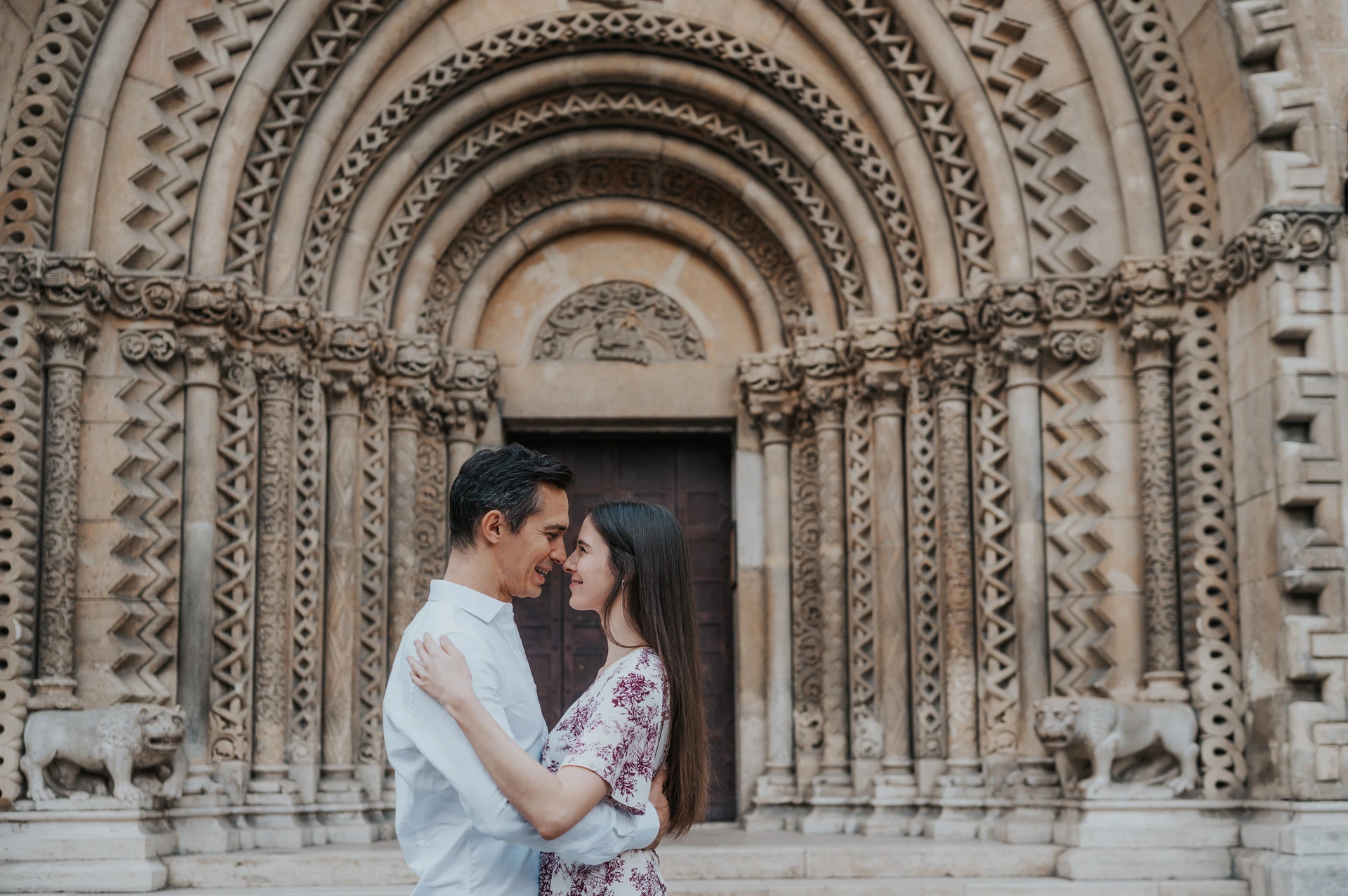 A wide portrait of the smiling couple embracing beneath Vajdahunyad Castle’s carved arches during their couple photoshoot in Budapest.