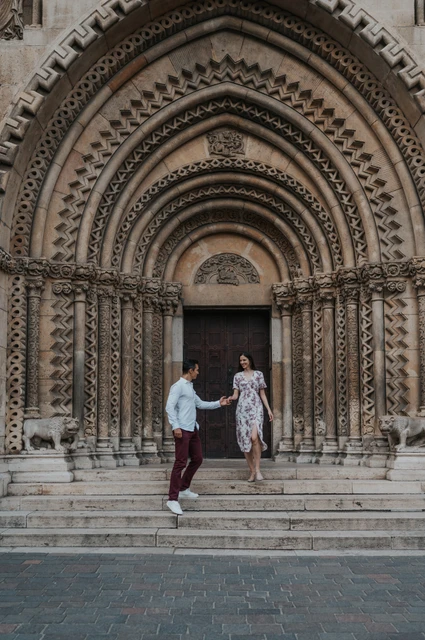 A walk down the castle steps at a Budapest couple photoshoot The couple stepping down together from Vajdahunyad Castle’s arched doorway during their couple photoshoot in Budapest.