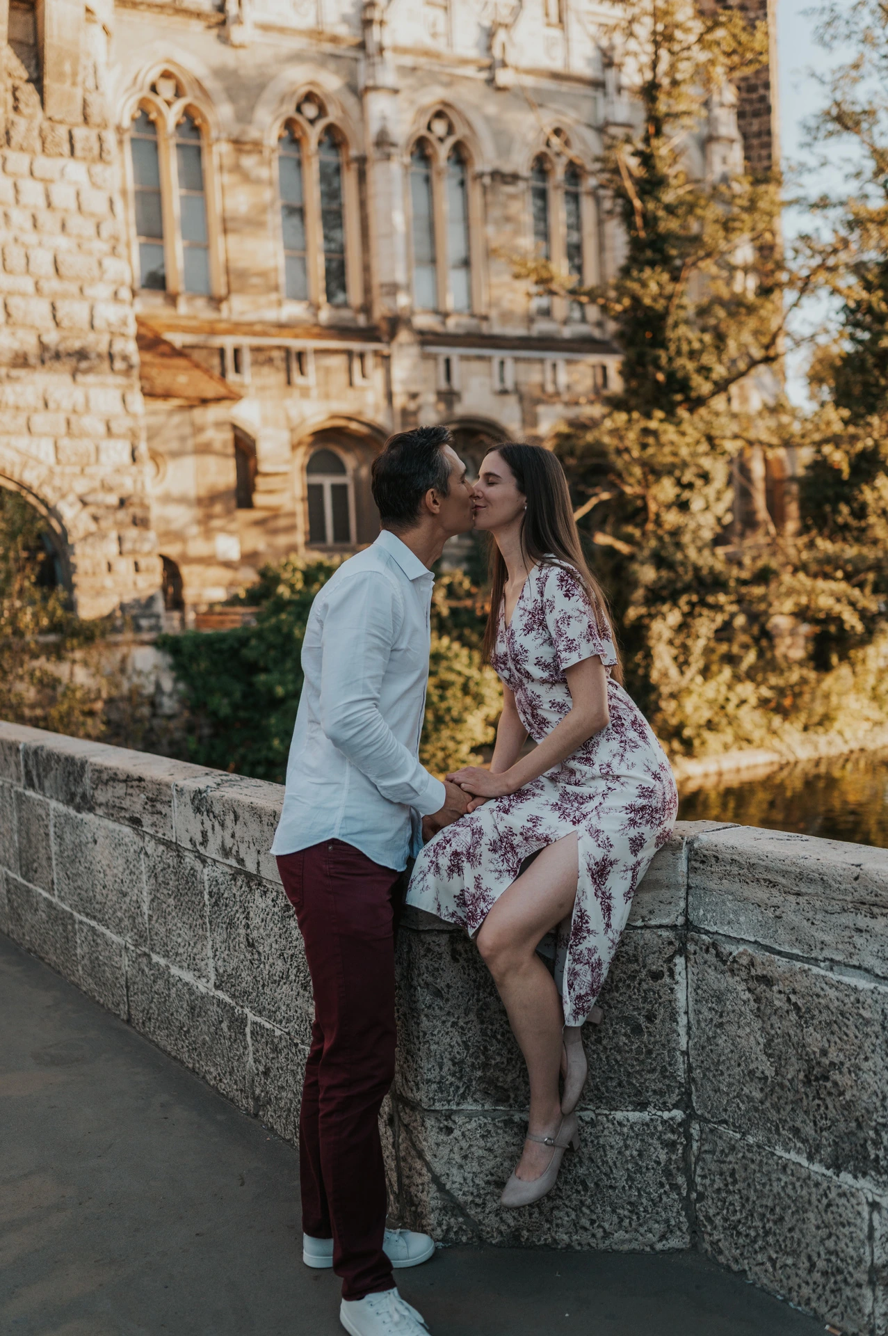 The couple embracing beside a low stone wall with Vajdahunyad Castle’s ornate palace façade and warm foliage behind them during their couple photoshoot in Budapest.