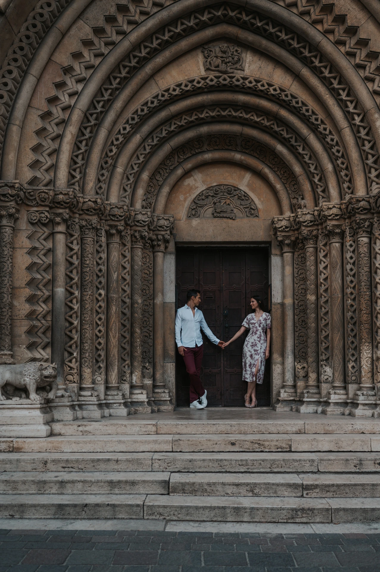 The couple holding hands on the steps beneath Vajdahunyad Castle’s ornate doorway during their couple photoshoot in Budapest.
