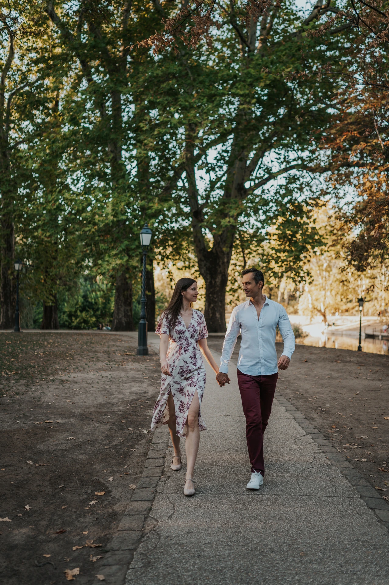 The couple walking towards the camera beneath the trees near Vajdahunyad Castle during their couple photoshoot in Budapest.