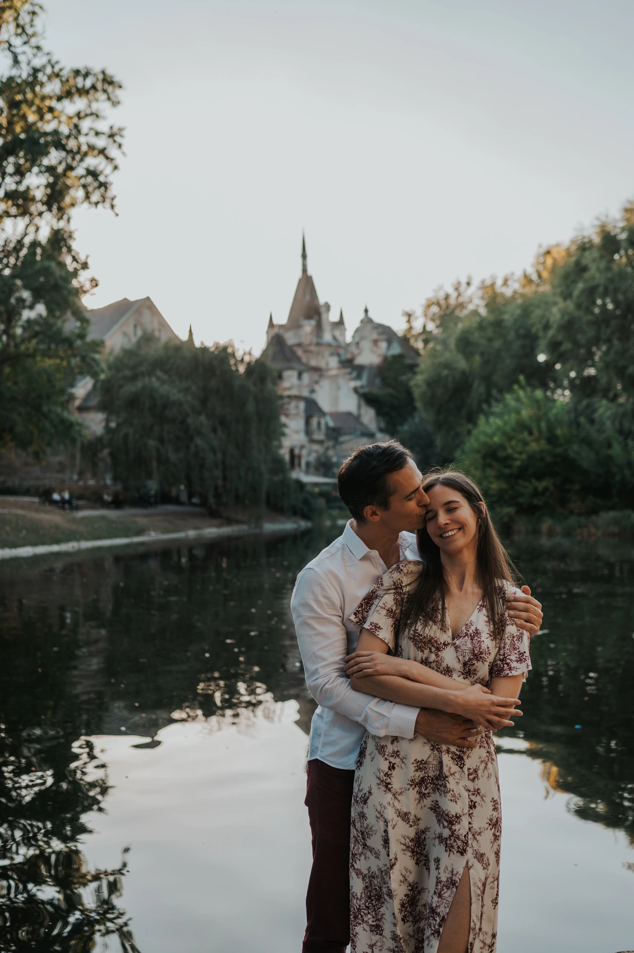 A close portrait of the couple smiling together beside the water with Vajdahunyad Castle’s turrets behind them during their couple photoshoot in Budapest.
