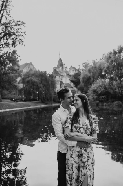 A waterside embrace in black and white at a Budapest couple photoshoot Black-and-white portrait of the couple embracing beside the water with Vajdahunyad Castle behind them during their couple photoshoot in Budapest.
