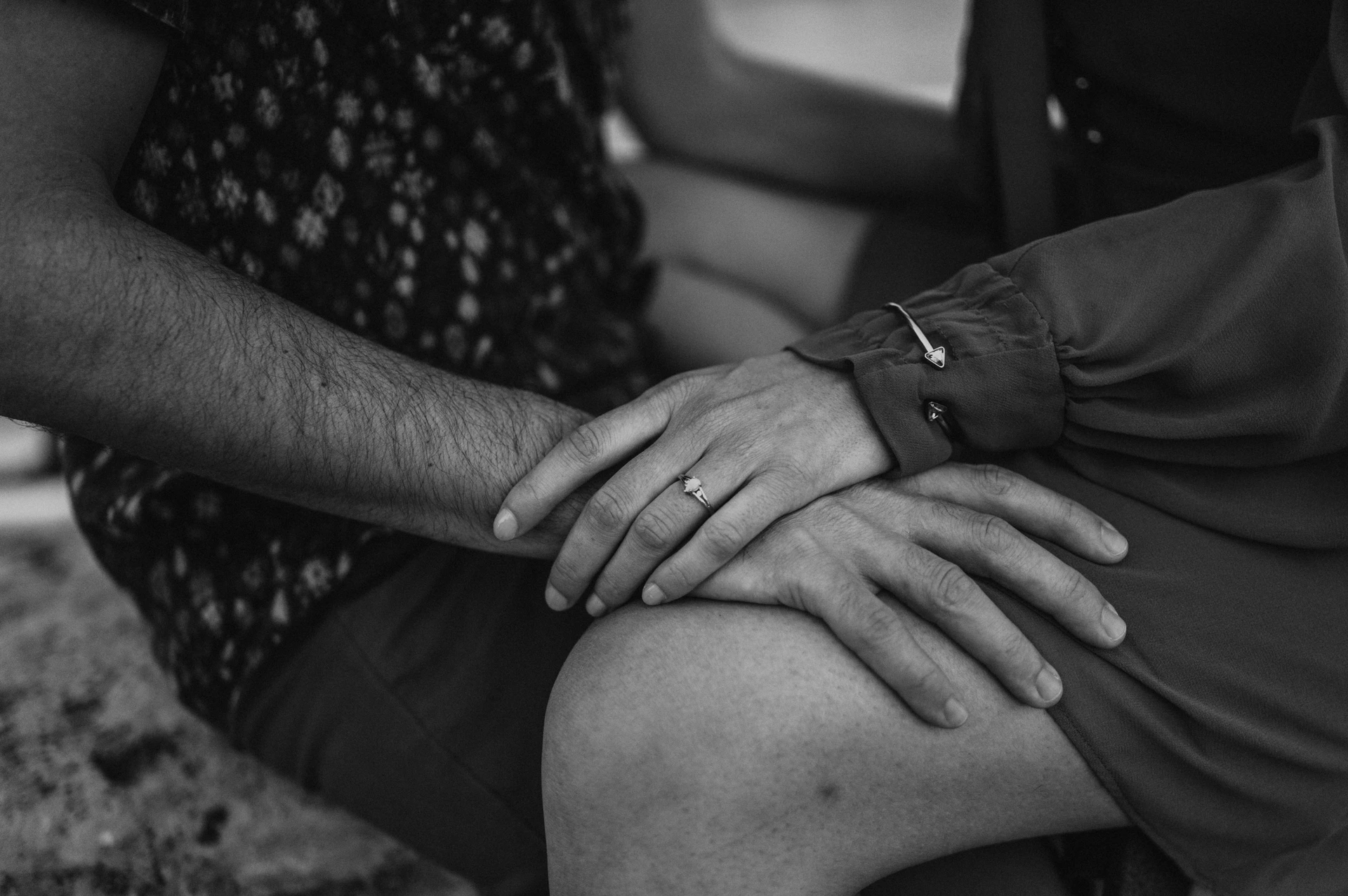 Black-and-white landscape close-up of the couple’s hands together on a lap, showing the engagement ring and the fabric of their outfits during their Budapest engagement photoshoot.
