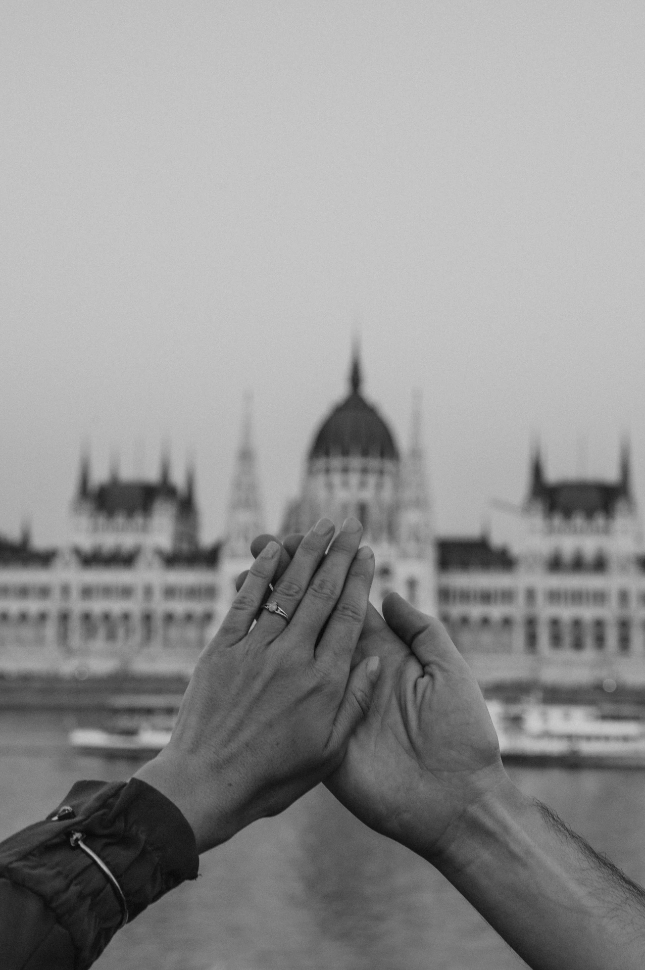 Budapest engagement photoshoot: A black-and-white ring portrait opposite Parliament Black-and-white close-up of the couple’s hands and engagement ring, with Parliament’s dome blurred in the background during their Budapest engagement photoshoot.
