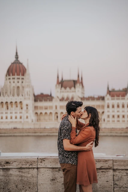 A closer portrait of the couple kissing beside the river wall, with Parliament’s dome and pointed towers softly behind them during their Budapest engagement photoshoot.