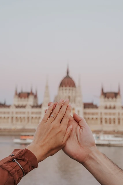 Budapest engagement photoshoot: A closer ring portrait with Parliament in the backdrop A closer photograph of the couple’s hands and engagement ring, framed by a softly blurred view of Parliament across the river during their Budapest engagement photoshoot.