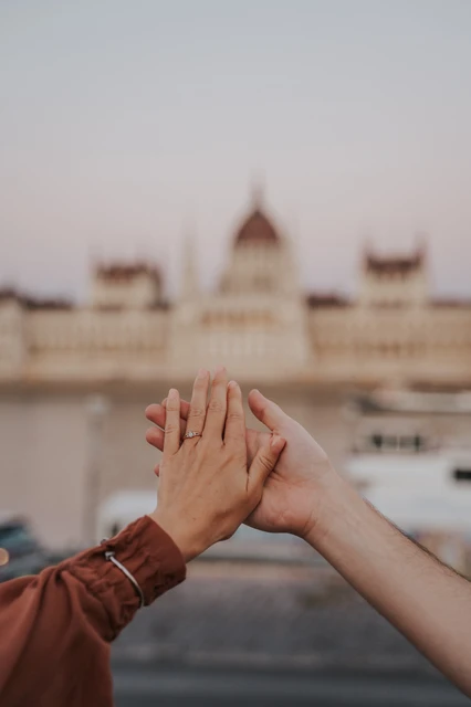 Budapest engagement photoshoot: Their engagement ring with Parliament beyond A close-up of the couple’s hands together and the engagement ring, with Parliament softly blurred across the Danube during their Budapest engagement photoshoot.