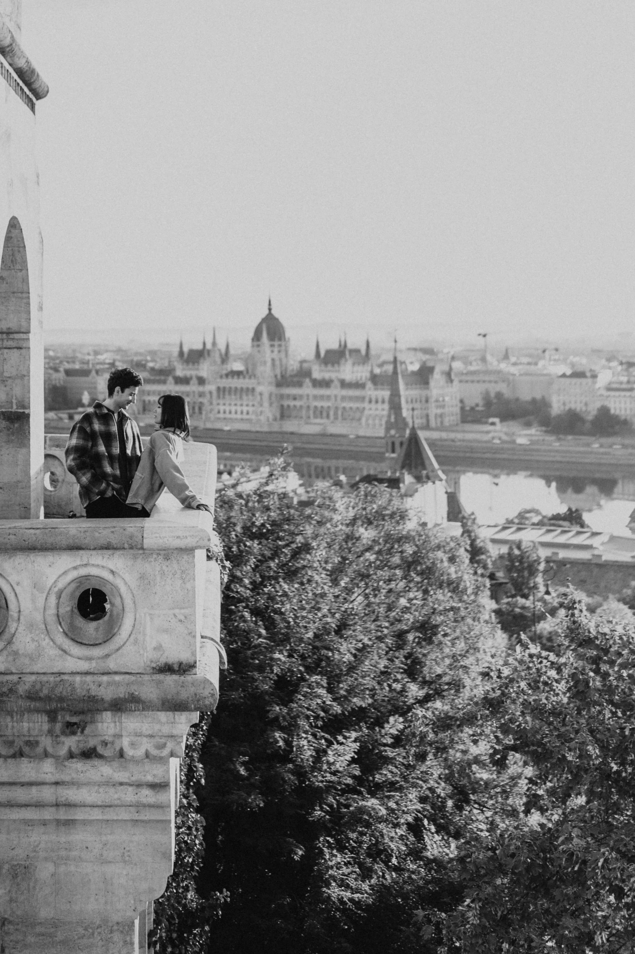 Black-and-white view of the couple on the Bastion balcony, with Parliament and the Danube in the background during their Budapest engagement photoshoot.