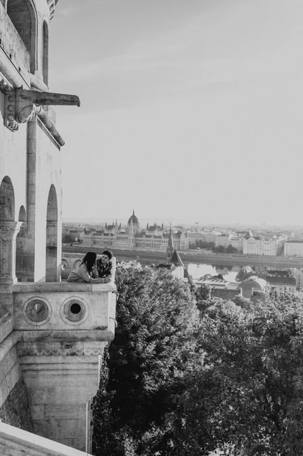 Budapest engagement photoshoot: a black-and-white kiss overlooking the city Black-and-white view of the couple kissing at the balcony corner, with Parliament and the river in the distance during their Budapest engagement photoshoot.