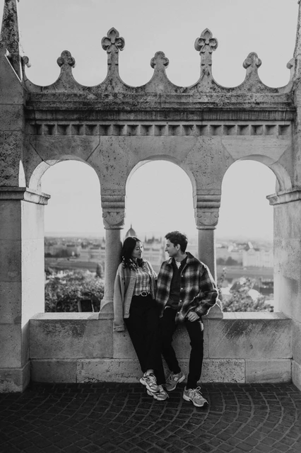 Budapest engagement photoshoot: a black-and-white portrait in the arcade Black-and-white portrait of the couple together beneath the decorative Bastion arches, with their relaxed outfits and trainers visible during their Budapest engagement photoshoot.