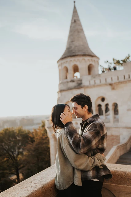 Budapest engagement photoshoot: a close kiss with her hand on his cheek A close portrait of the couple kissing beside the stone balustrade, with her hand resting against his cheek during their Budapest engagement photoshoot.