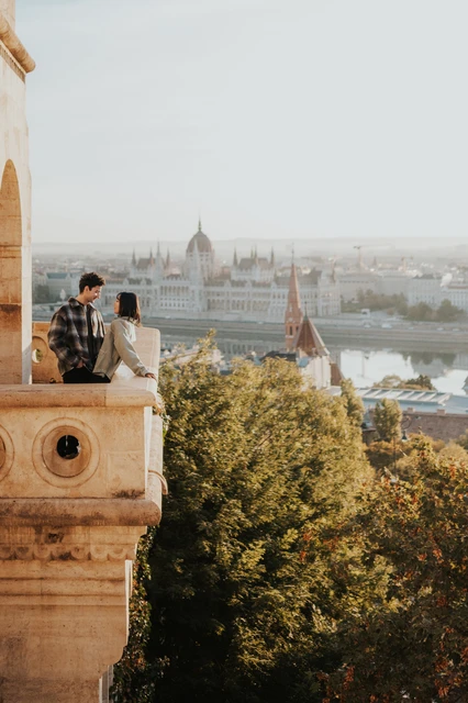 The couple close together on the corner of the stone balcony at Fisherman’s Bastion, with Parliament across the river behind them during their Budapest engagement photoshoot.