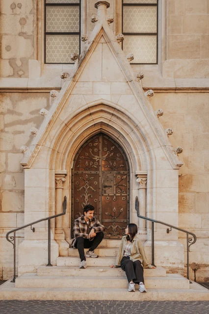 Budapest engagement photoshoot: a closer view of the couple on the steps A closer vertical view of the couple seated on the doorway steps, with their casual outfits and trainers in view during their Budapest engagement photoshoot.