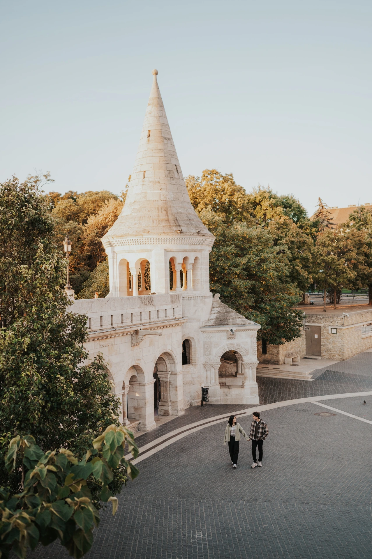 An elevated view of the couple walking together across the paved lower terrace beside Fisherman’s Bastion during their Budapest engagement photoshoot.