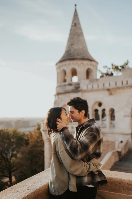 Budapest engagement photoshoot: a warm embrace beside the tower The couple embracing and kissing on the Bastion terrace, with their coordinated casual clothing and the pale tower behind them during their Budapest engagement photoshoot.