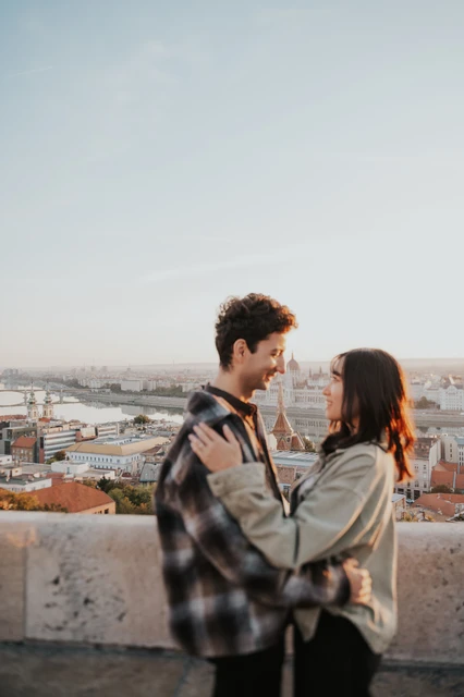 Budapest engagement photoshoot: an embrace beside the city-view terrace The couple standing close together beside the stone terrace wall at Fisherman’s Bastion, with Budapest in the background during their Budapest engagement photoshoot.