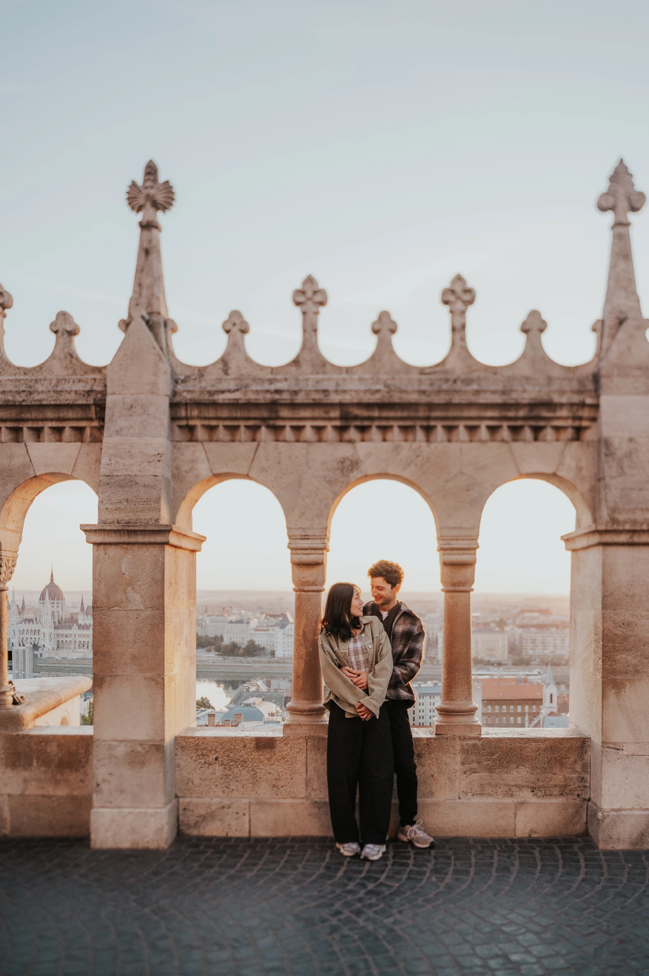 The couple embracing beneath the central arch at Fisherman’s Bastion, with the ornate stone arcade above them during their Budapest engagement photoshoot.