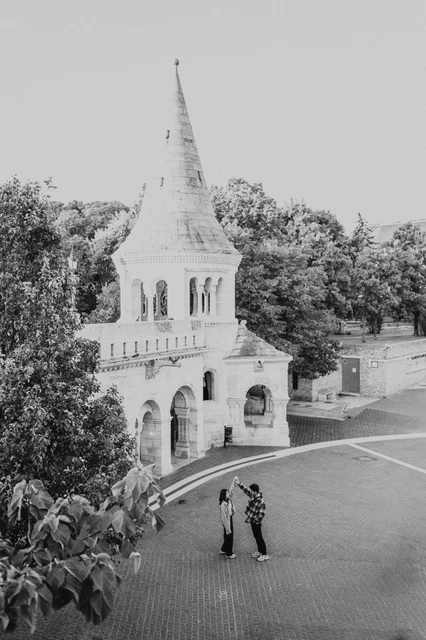 Budapest engagement photoshoot: black-and-white architecture and two figures Black-and-white elevated view of the couple on the paving near the lower Bastion tower and surrounding trees during their Budapest engagement photoshoot.