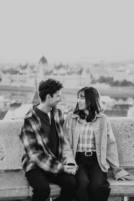 Budapest engagement photoshoot: black-and-white smiles overlooking Parliament Black-and-white portrait of the couple holding hands on the bench at Fisherman’s Bastion, with Parliament in the distance during their Budapest engagement photoshoot.