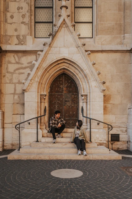 Budapest engagement photoshoot: casual portraits on the doorway steps The couple sitting on different levels of the stone steps beneath an ornate wooden door and pointed stone arch during their Budapest engagement photoshoot.
