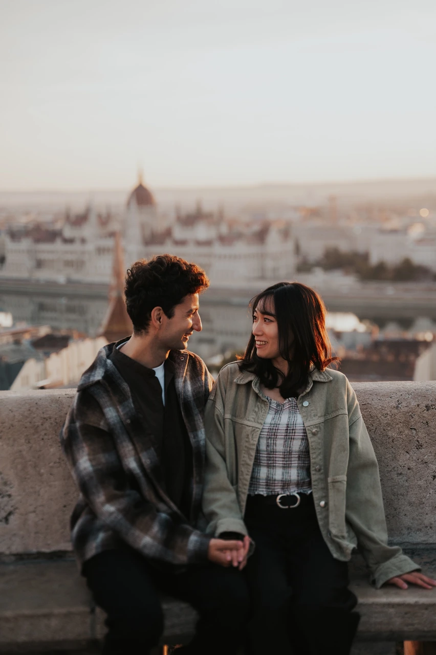 Budapest engagement photoshoot: close smiles with Parliament in the backdrop A close portrait of the couple smiling at one another on the stone bench, with the Hungarian Parliament softly blurred behind them during their Budapest engagement photoshoot.