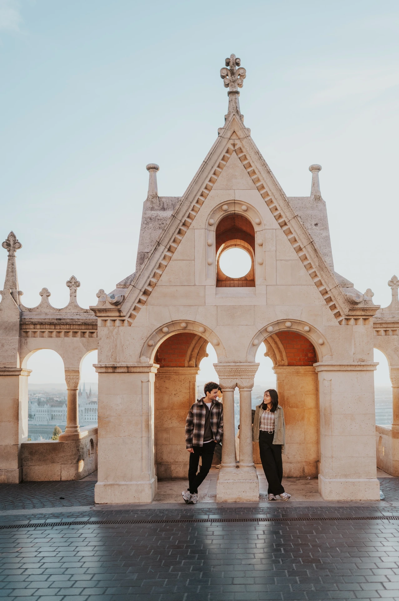 The couple standing on either side of a pointed stone arch at Fisherman’s Bastion, with decorative stonework above them during their Budapest engagement photoshoot.
