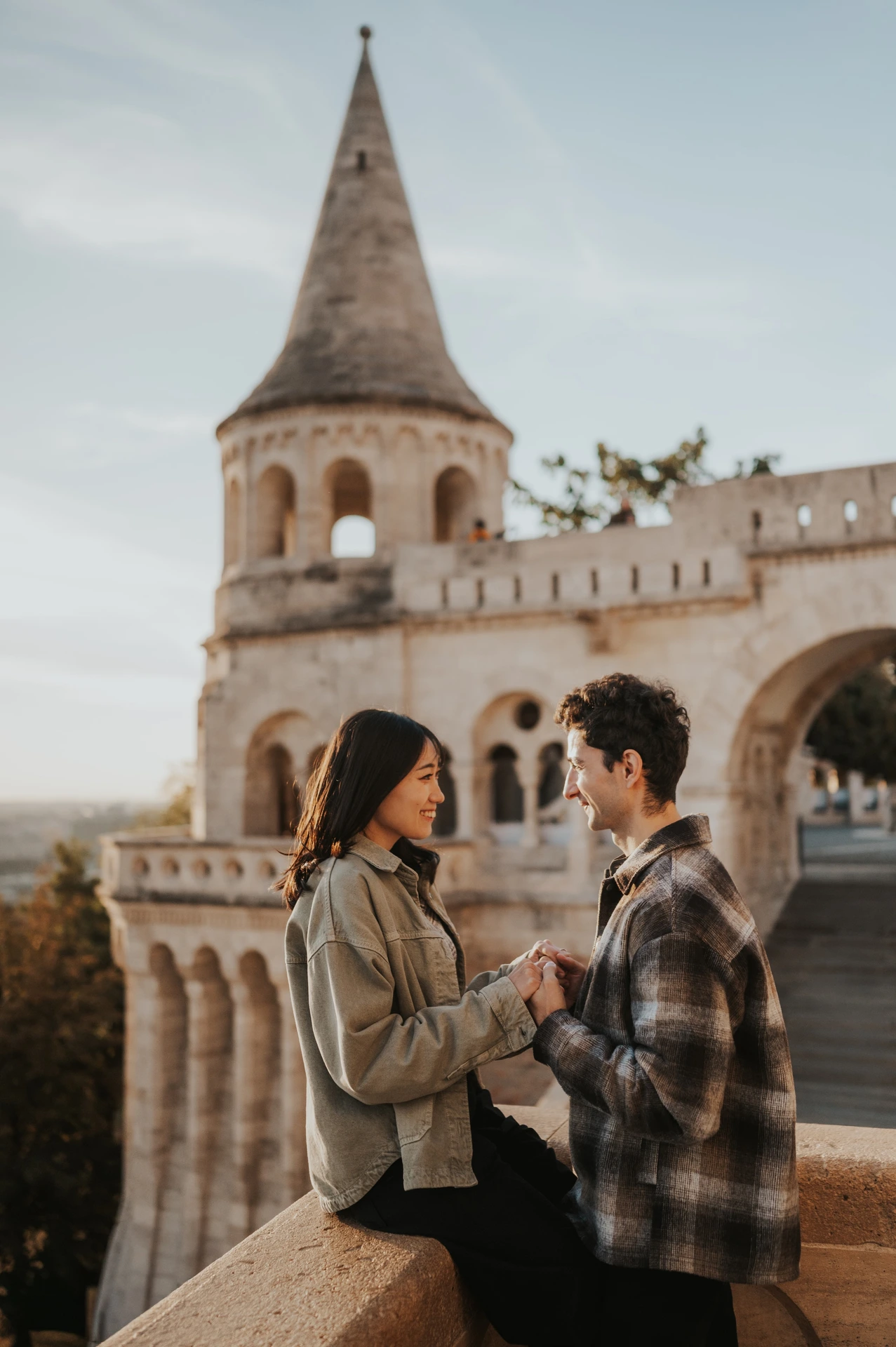 The couple smiling towards one another beside the curved stone railing at Fisherman’s Bastion during their Budapest engagement photoshoot.