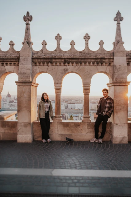 Budapest engagement photoshoot: standing beneath separate stone arches The couple standing apart beneath the decorative stone arches at Fisherman’s Bastion, with warm morning light coming through the openings during their Budapest engagement photoshoot.
