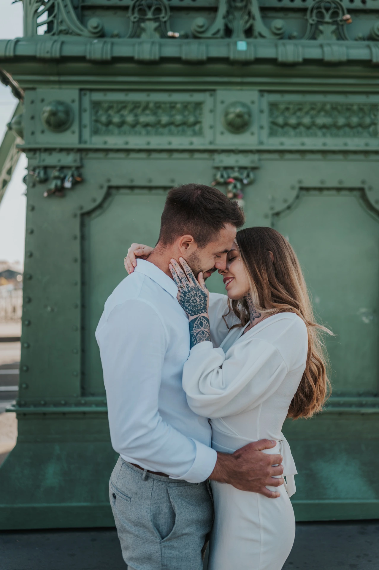 The couple resting their foreheads together in front of an ornate green lamp-post base on Liberty Bridge during their engagement photoshoot in Budapest.