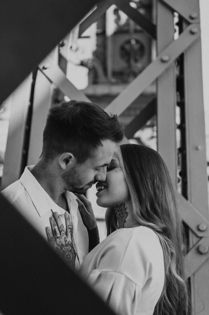 A framed bridge portrait in black and white | Budapest engagement photoshoot Black-and-white photograph of the couple resting their foreheads together, framed by the steel beams of Liberty Bridge during their engagement photoshoot in Budapest.