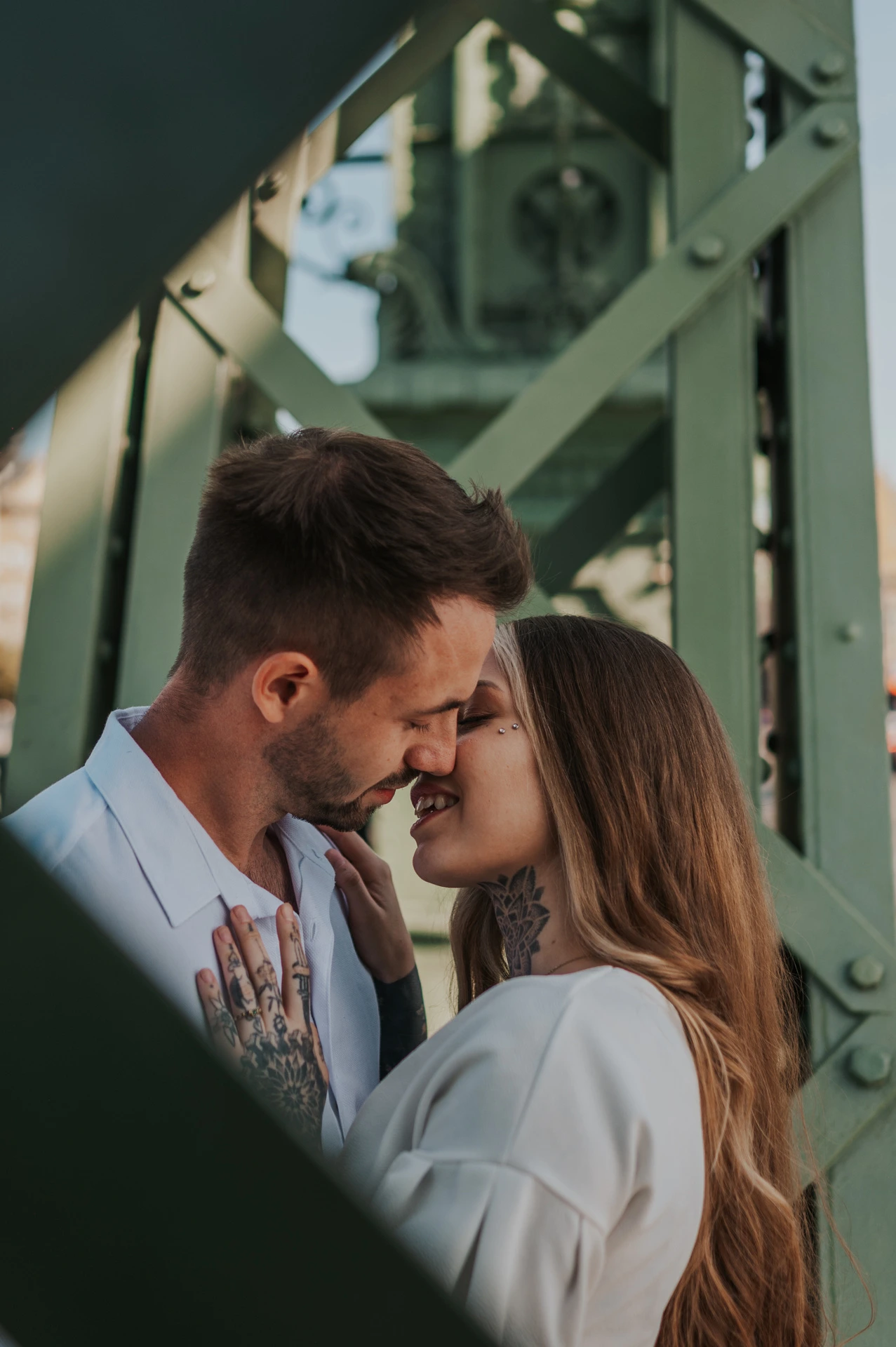The couple smiling with their foreheads together, framed by the green steel beams of Liberty Bridge during their engagement photoshoot in Budapest.