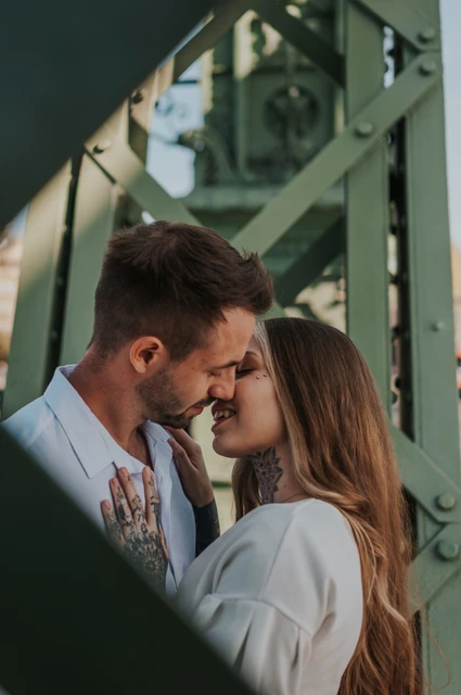 A portrait framed by the green steel beams | Budapest engagement photoshoot The couple smiling with their foreheads together, framed by the green steel beams of Liberty Bridge during their engagement photoshoot in Budapest.