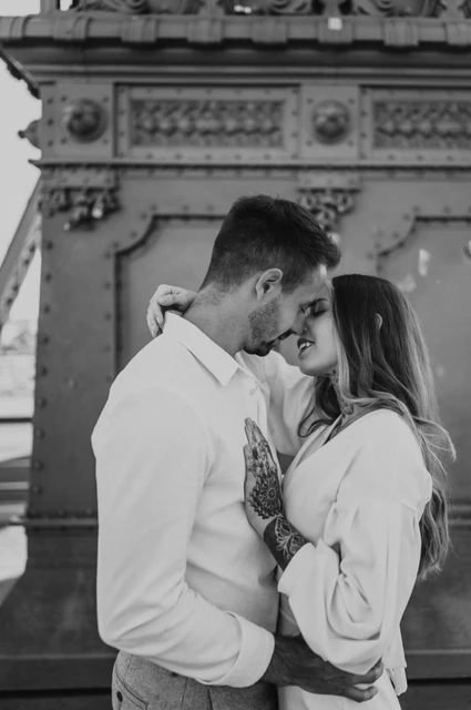 A kiss by the lamp-post in black and white | Budapest engagement photoshoot Black-and-white photograph of the couple kissing in front of an ornate lamp-post base on Liberty Bridge during their engagement photoshoot in Budapest.
