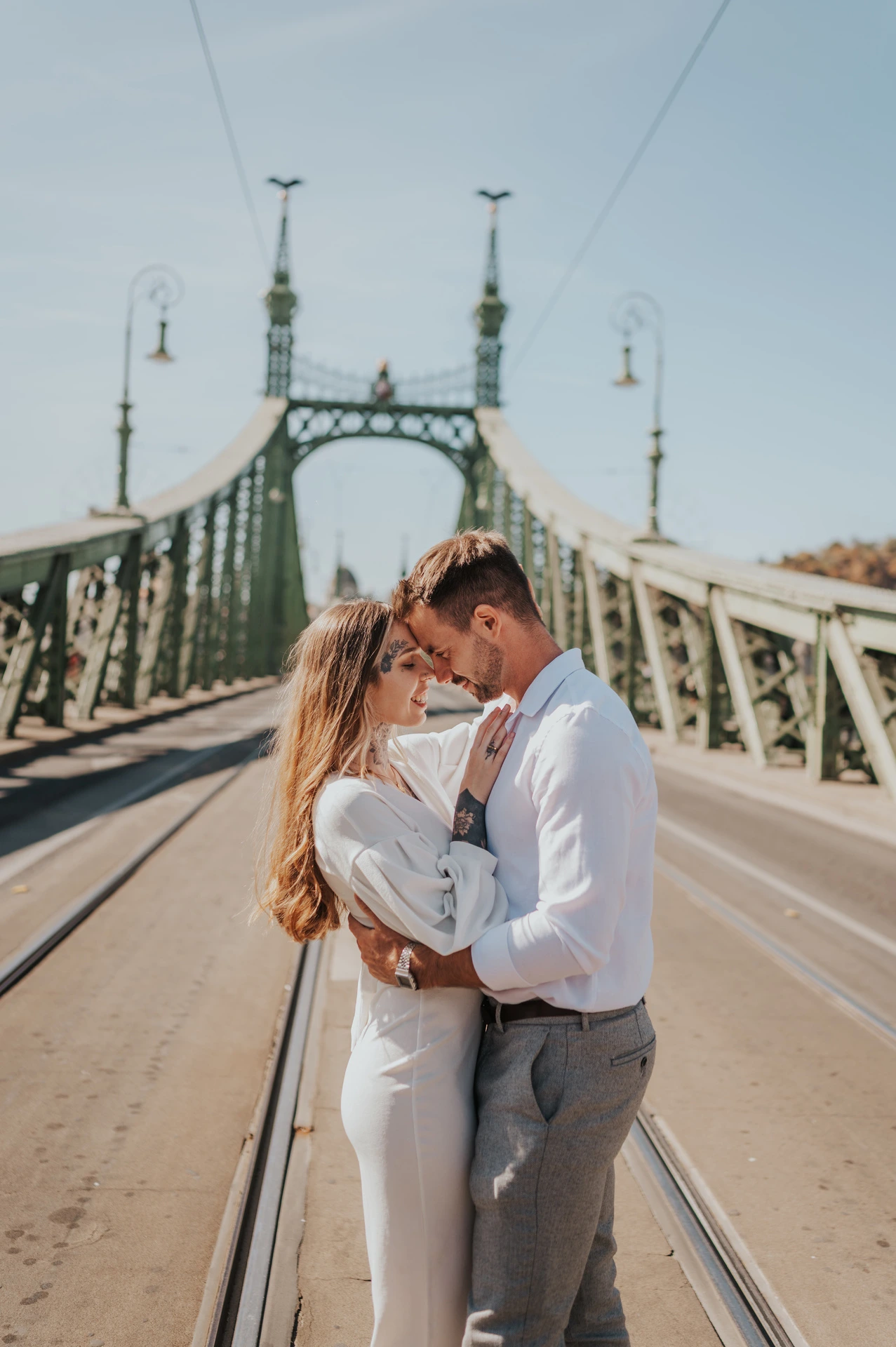 The couple resting their foreheads together with the green towers of Liberty Bridge rising behind them during their engagement photoshoot in Budapest.