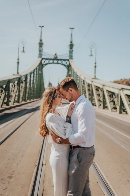 A close portrait with the bridge towers behind them | Budapest engagement photoshoot The couple resting their foreheads together with the green towers of Liberty Bridge rising behind them during their engagement photoshoot in Budapest.