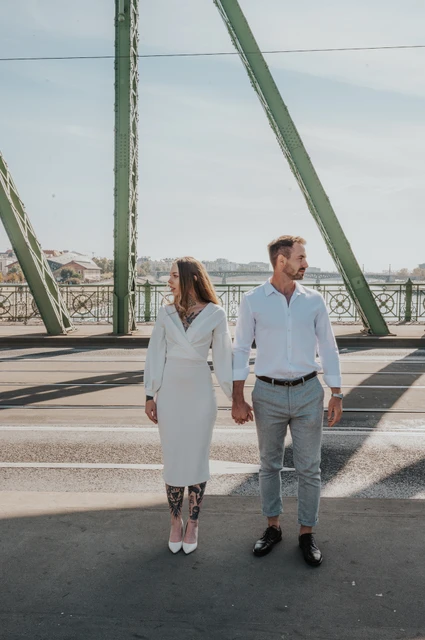 A walk together along Liberty Bridge | Budapest engagement photoshoot The couple walking hand in hand along Liberty Bridge, with green steel beams around them during their engagement photoshoot in Budapest.
