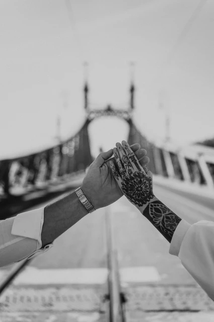 Their ring and bridge backdrop in black and white | Budapest engagement photoshoot Black-and-white photograph of a close-up of the couple’s hands showing their engagement ring and tattoos, with Liberty Bridge softly blurred behind them during their engagement photoshoot in Budapest.