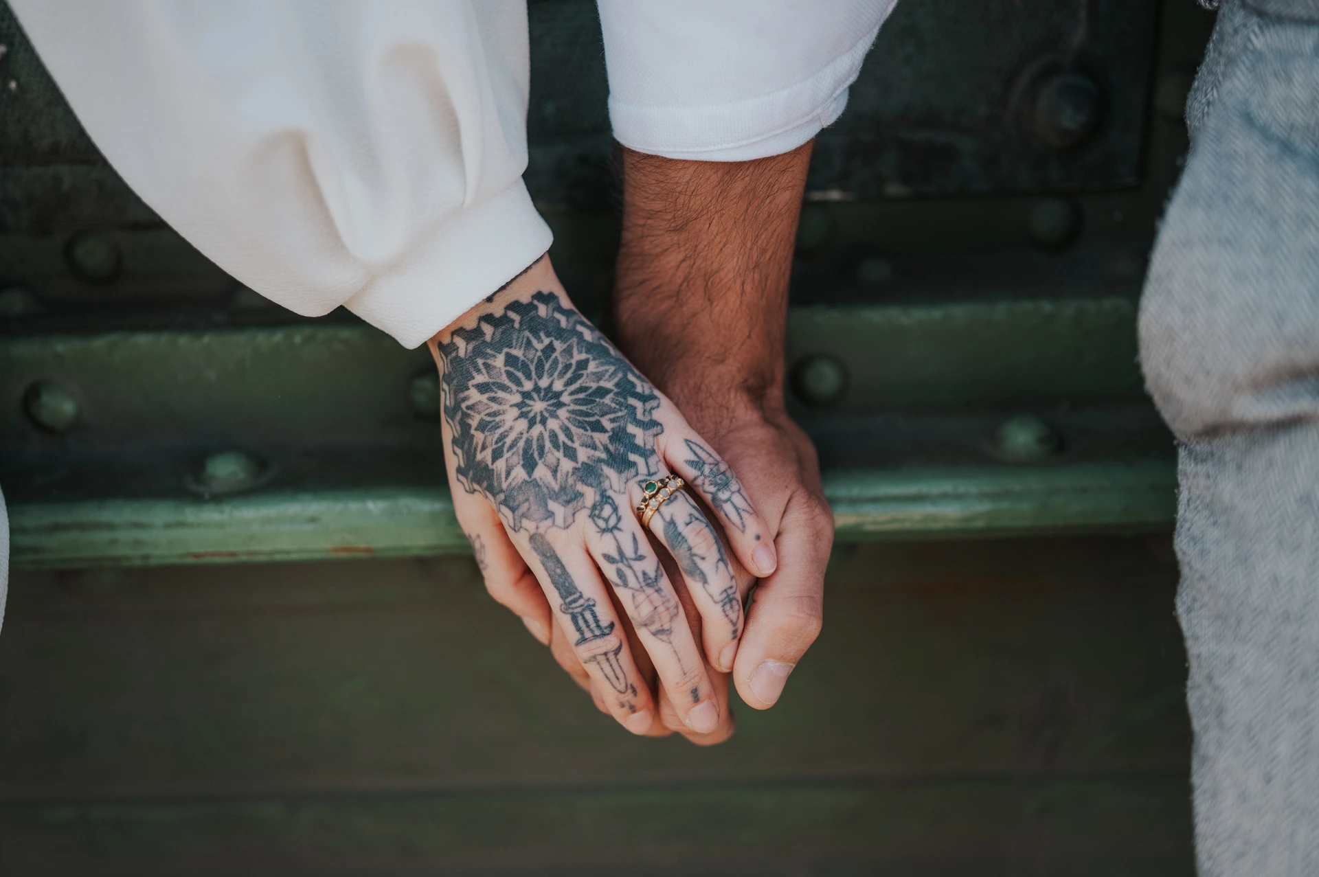 Tattoo details and hands together | Budapest engagement photoshoot A wide close-up of the couple’s hands resting together, with their tattoos and white sleeves against green bridge steelwork during their engagement photoshoot in Budapest.