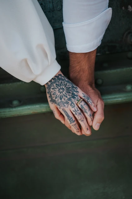 Their hands and tattoos against the green bridge | Budapest engagement photoshoot A close portrait of the couple’s hands resting together, with tattoo details and white sleeves against the green bridge during their engagement photoshoot in Budapest.
