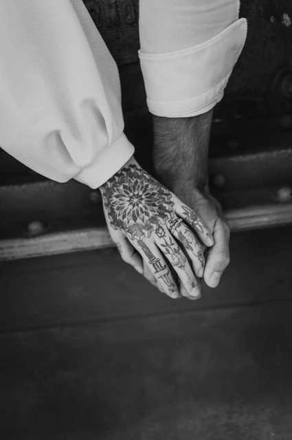 A close hand portrait in black and white | Budapest engagement photoshoot Black-and-white photograph of a close portrait of the couple’s tattooed hands and white sleeves against the bridge steelwork during their engagement photoshoot in Budapest.